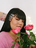 Woman with four barrettes in three-quarters profile holding two pink, blooming roses