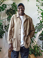 A smiling, older man in a khaki jacket facing the camera in his indoor garden