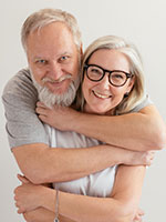 A happy, grey-haired couple facing the camera with their arms wrapped tightly around each other