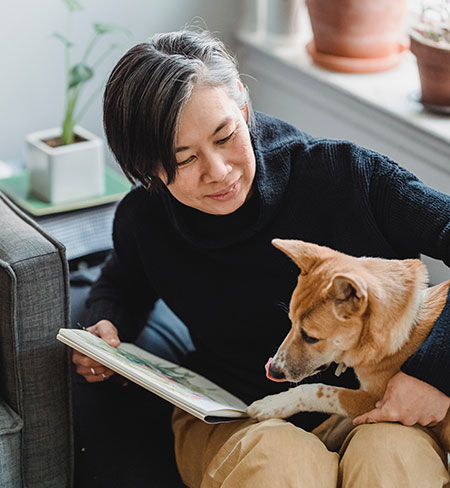Grey-haired East-Asian woman holding a sketchpad and her dog on her lap