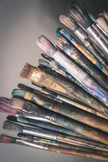 Well-loved paintbrushes fanned out in an arc, each covered in dried, winter-hued paints
